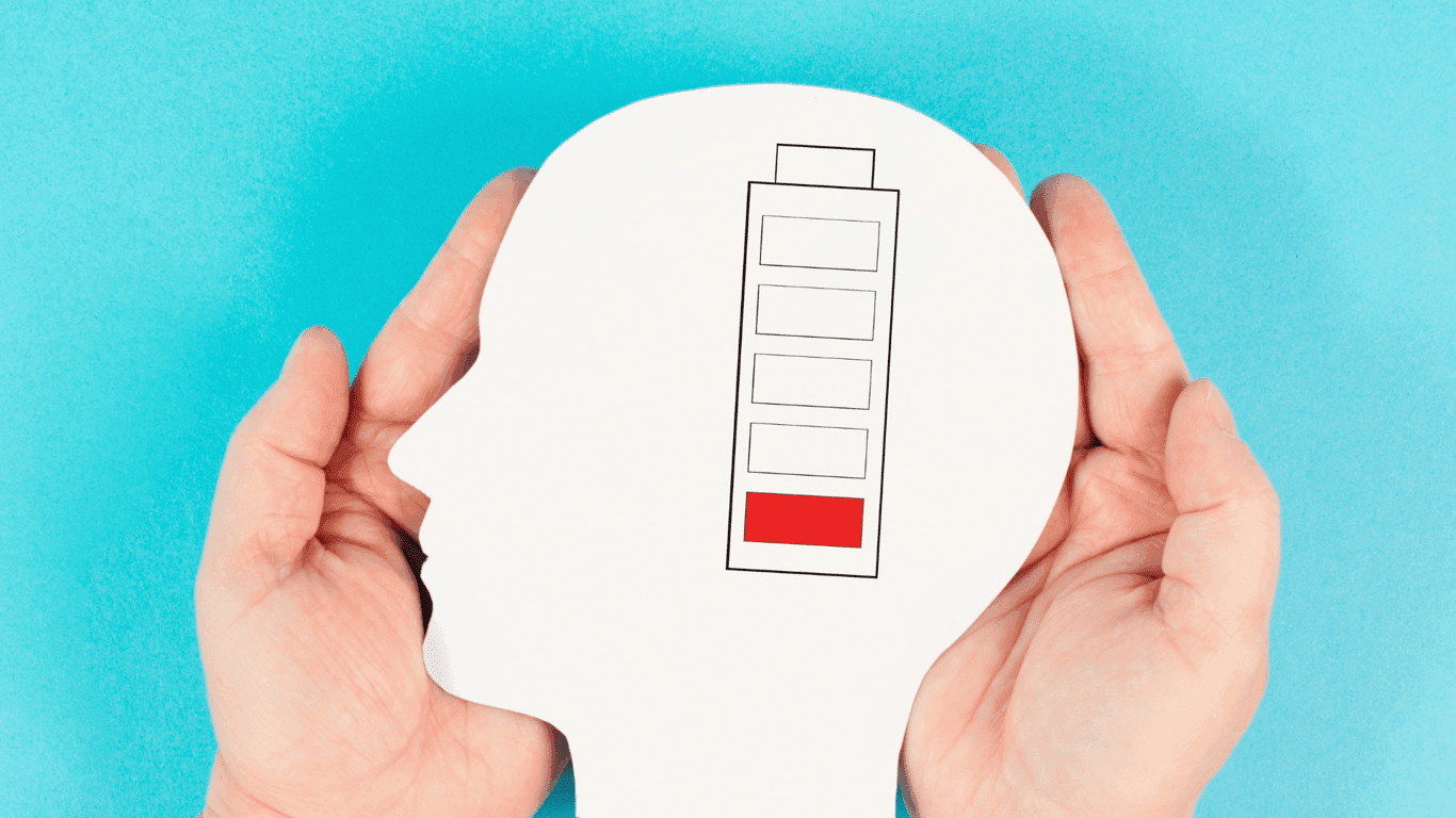 Låg batterinivå illustrerad med ett gammalt batteri i en vit silhuett i form av ett huvud i profil, bilden är utskuren och ligger mellan två händer.